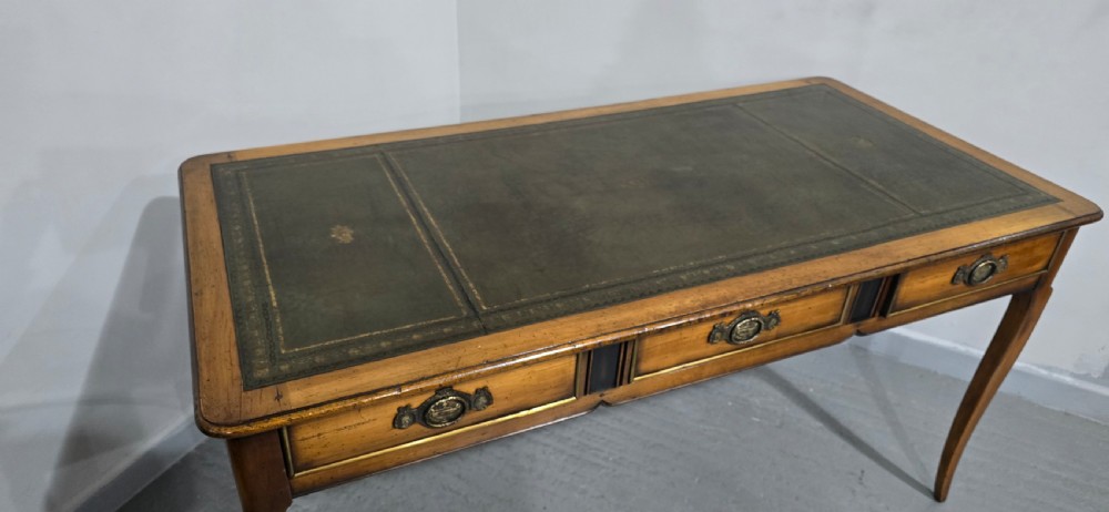 A French style warm oak library desk featuring a green leather inset writing surface, three frieze drawers with decorative brass handles, and slender cabriole legs. View VIII