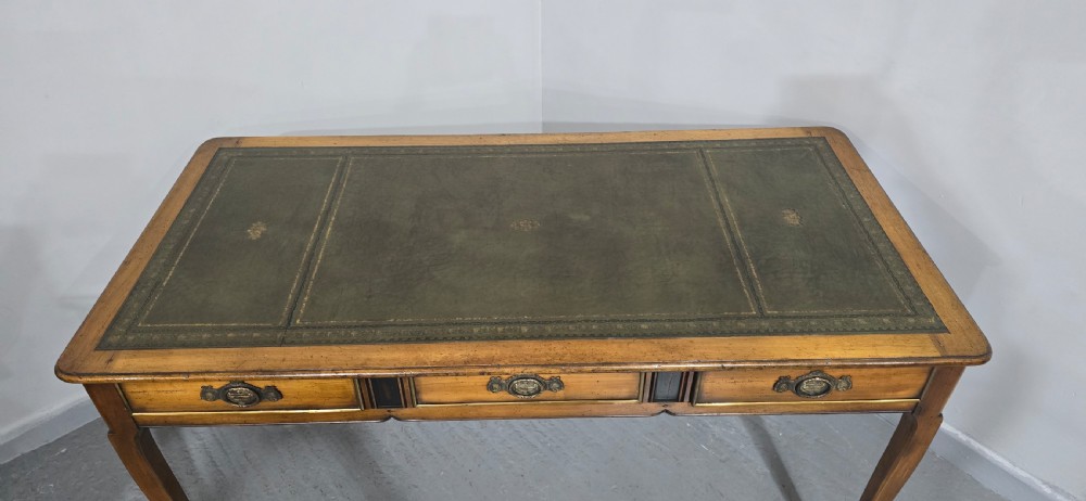 A French style warm oak library desk featuring a green leather inset writing surface, three frieze drawers with decorative brass handles, and slender cabriole legs. View IX