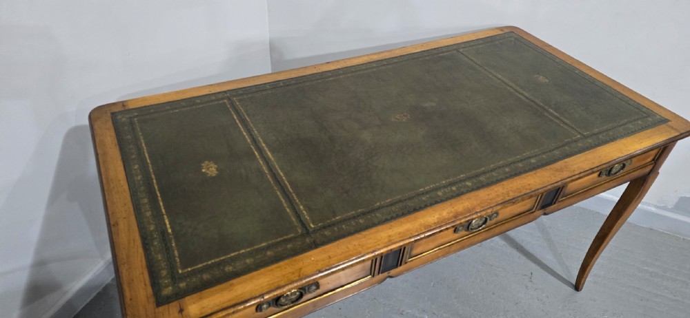 A French style warm oak library desk featuring a green leather inset writing surface, three frieze drawers with decorative brass handles, and slender cabriole legs. View XII