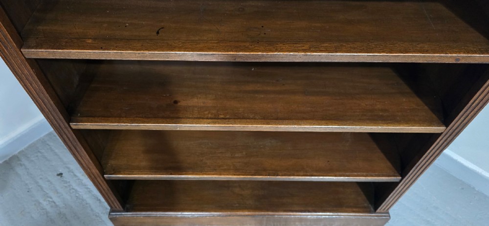 An antique oak open bookcase featuring four adjustable shelves filled with leather-bound books, twin drawers with brass handles, and fluted column side details. View XII