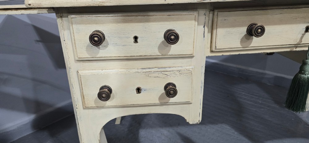 A cream painted French kneehole desk featuring a black leather inset writing surface, curved cabriole legs, and brass drawer knobs with a key and tassel hanging from the central drawer. View XII