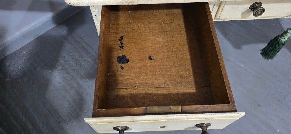 A cream painted French kneehole desk featuring a black leather inset writing surface, curved cabriole legs, and brass drawer knobs with a key and tassel hanging from the central drawer. View XIII