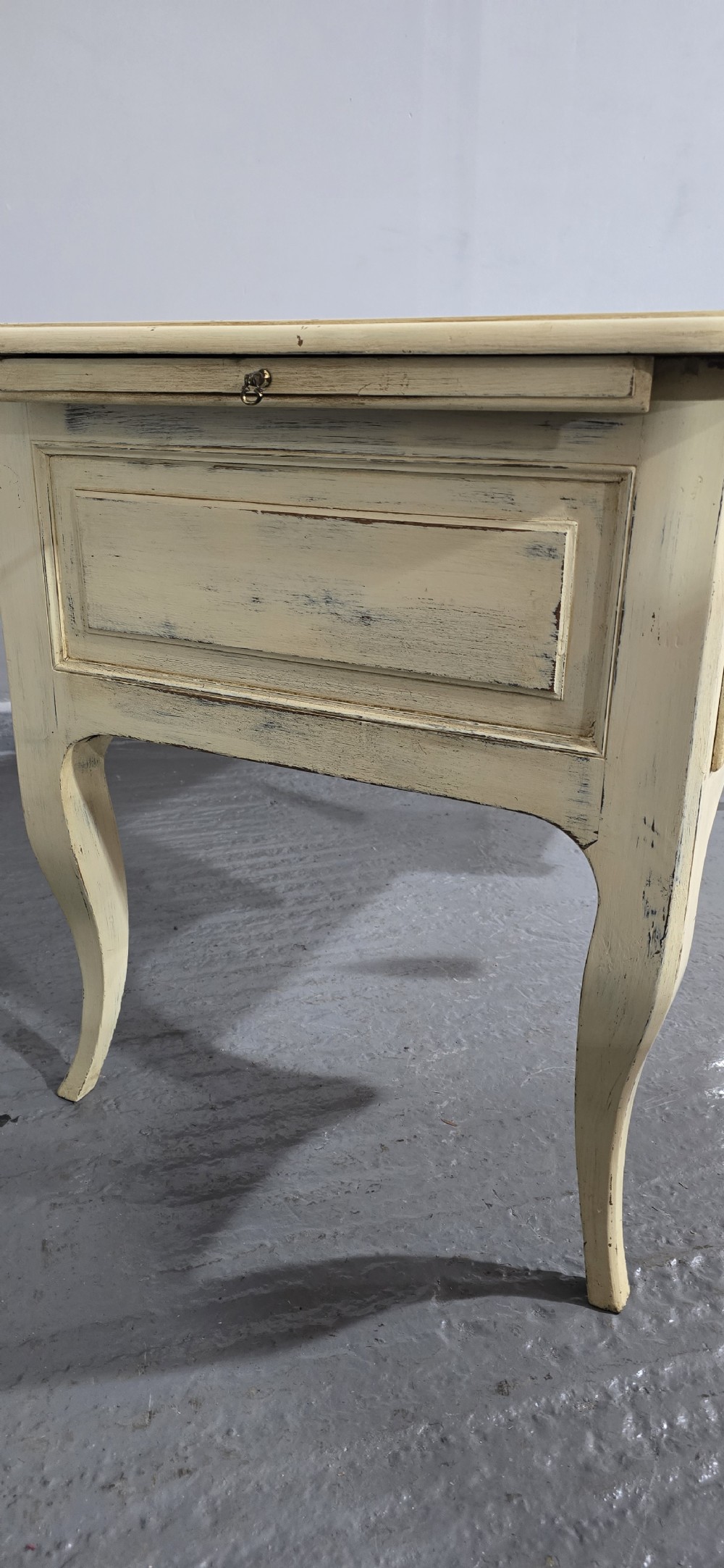 A cream painted French kneehole desk featuring a black leather inset writing surface, curved cabriole legs, and brass drawer knobs with a key and tassel hanging from the central drawer. View XVI