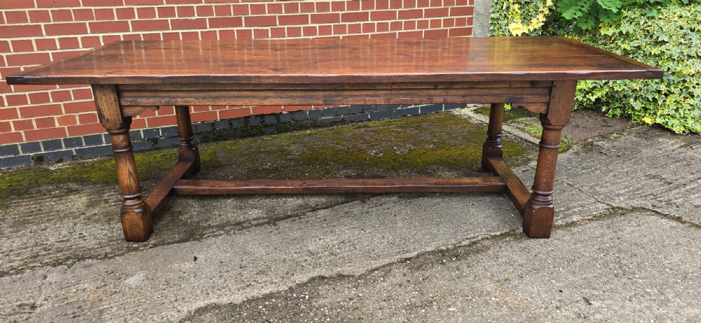 A long solid oak refectory dining table featuring a plank top, turned legs, and a low stretcher base. View V