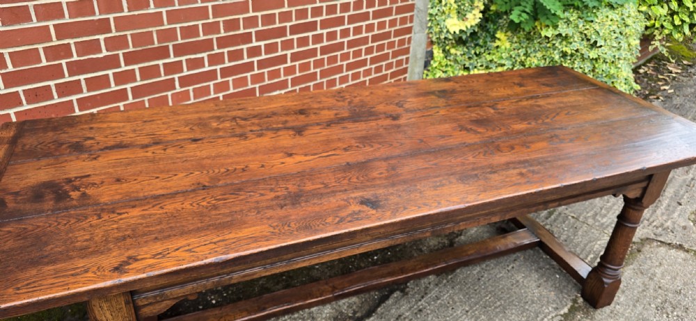 A long solid oak refectory dining table featuring a plank top, turned legs, and a low stretcher base. View IX