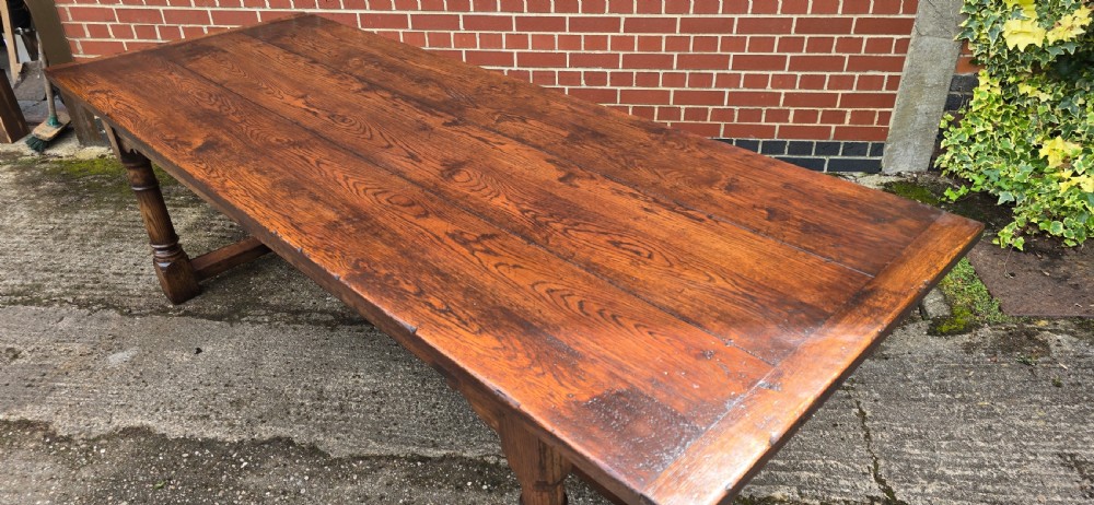 A long solid oak refectory dining table featuring a plank top, turned legs, and a low stretcher base. View X