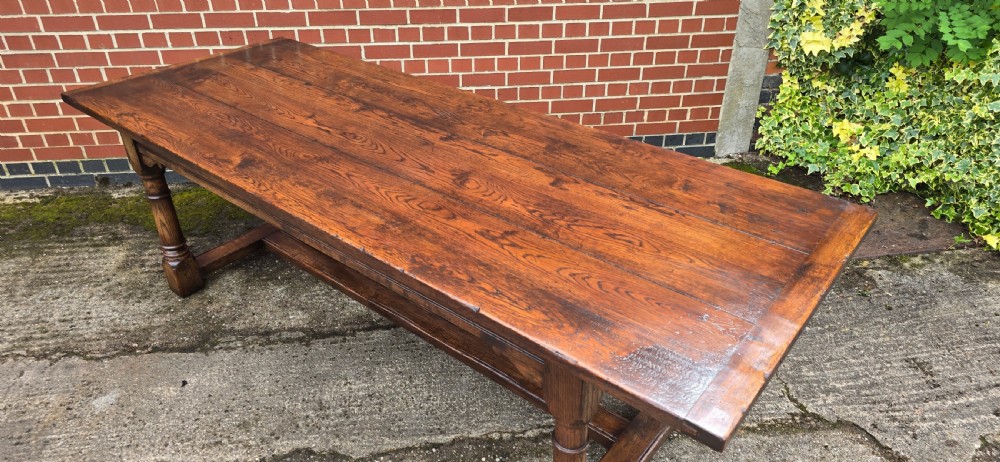 A long solid oak refectory dining table featuring a plank top, turned legs, and a low stretcher base. View XI