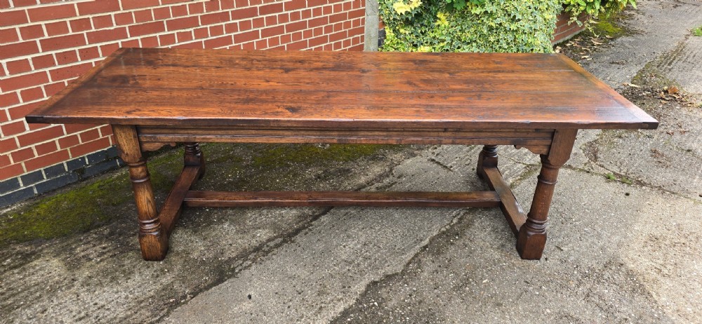 A long solid oak refectory dining table featuring a plank top, turned legs, and a low stretcher base. View XII