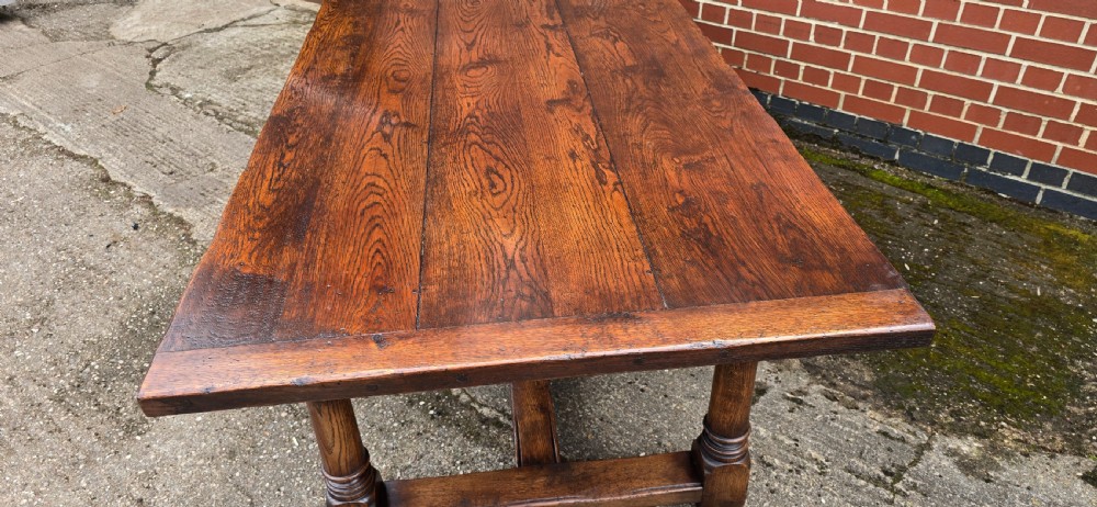 A long solid oak refectory dining table featuring a plank top, turned legs, and a low stretcher base. View XV