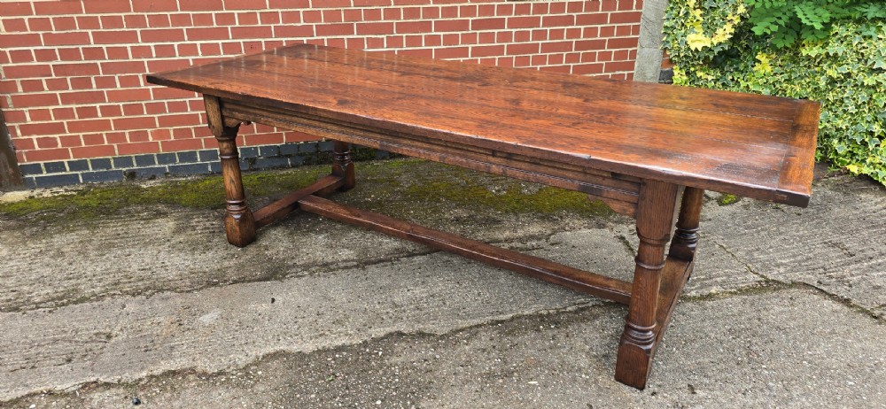 A long solid oak refectory dining table featuring a plank top, turned legs, and a low stretcher base. View XVII