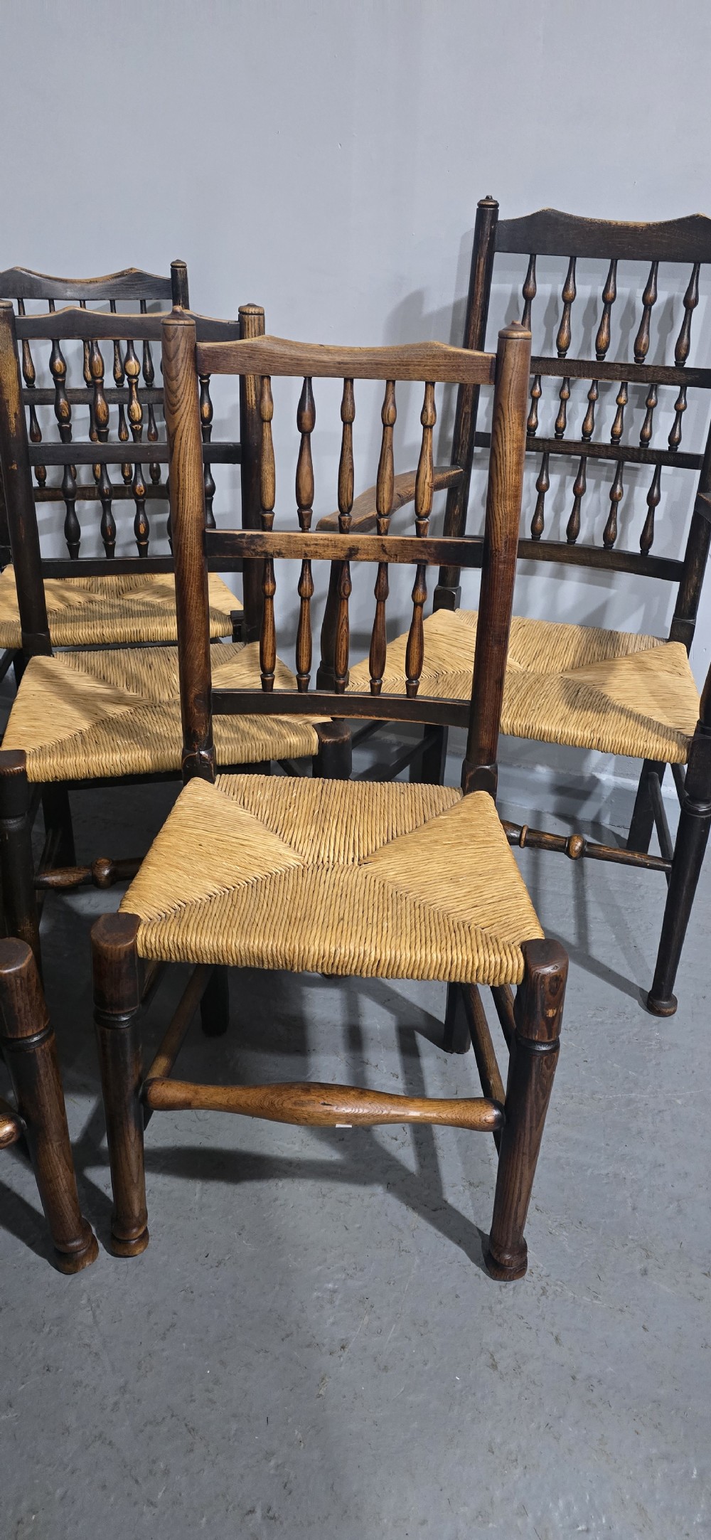 A harlequin set of eight dark oak spindle back dining chairs featuring woven rush seats, turned legs, and stretchers. View IV