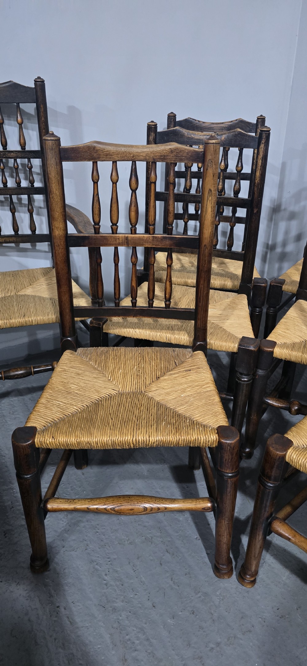 A harlequin set of eight dark oak spindle back dining chairs featuring woven rush seats, turned legs, and stretchers. View V