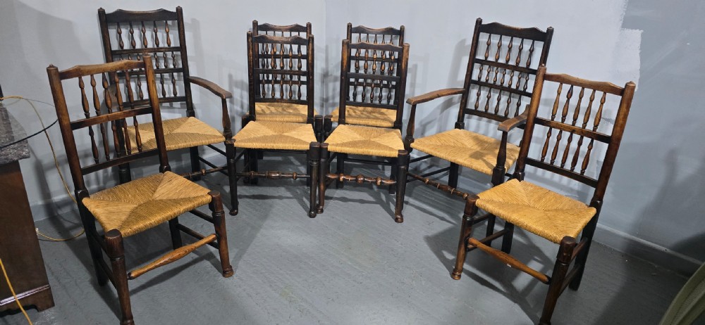 A harlequin set of eight dark oak spindle back dining chairs featuring woven rush seats, turned legs, and stretchers. View VI