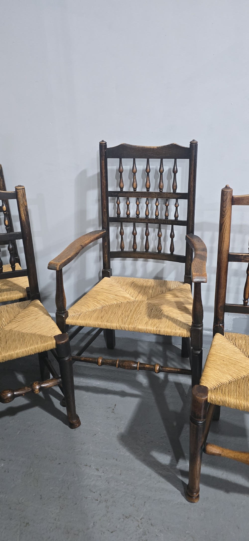 A harlequin set of eight dark oak spindle back dining chairs featuring woven rush seats, turned legs, and stretchers. View VIII