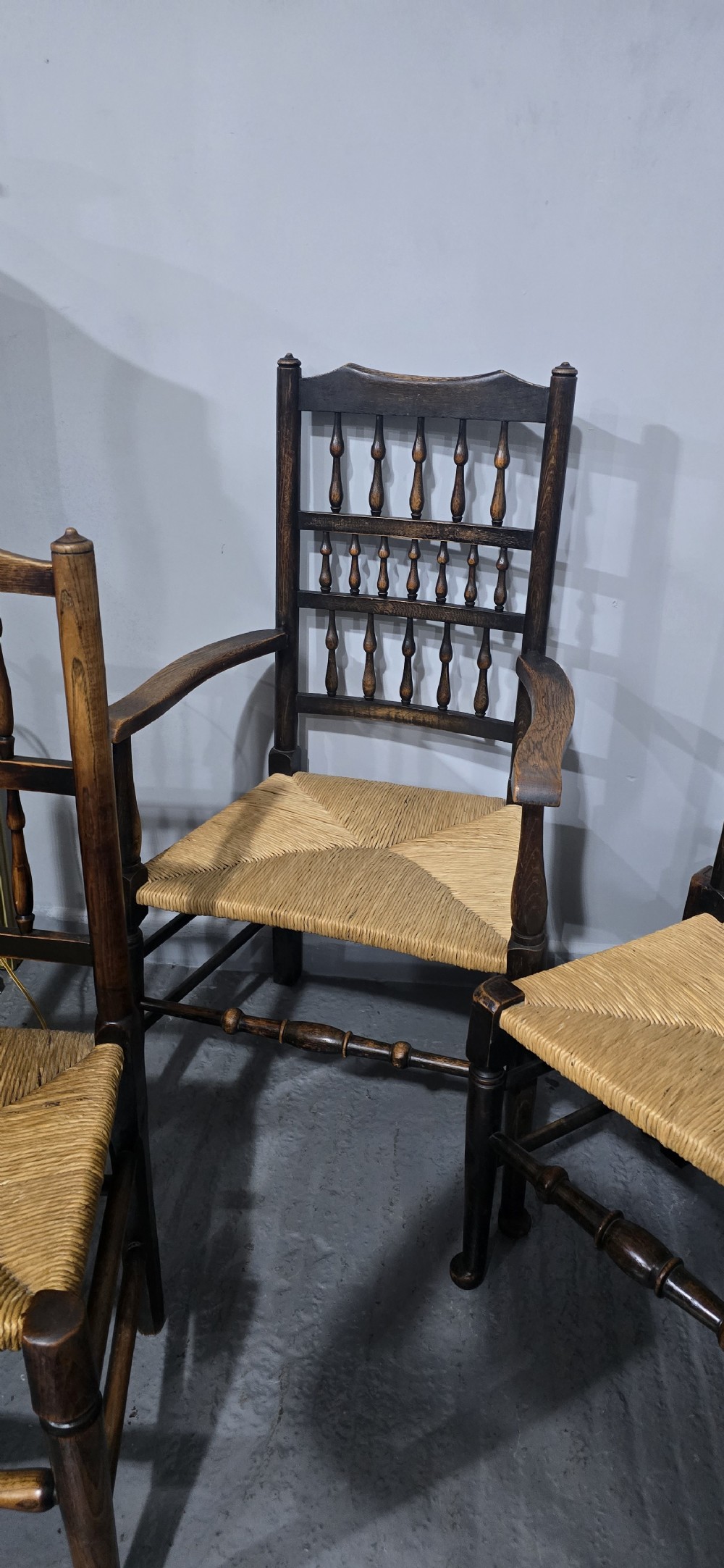 A harlequin set of eight dark oak spindle back dining chairs featuring woven rush seats, turned legs, and stretchers. View IX