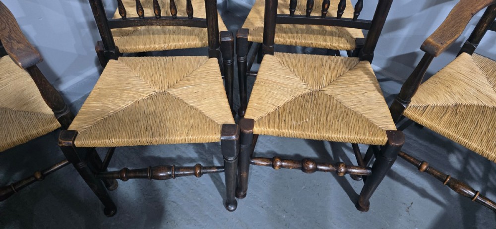 A harlequin set of eight dark oak spindle back dining chairs featuring woven rush seats, turned legs, and stretchers. View X