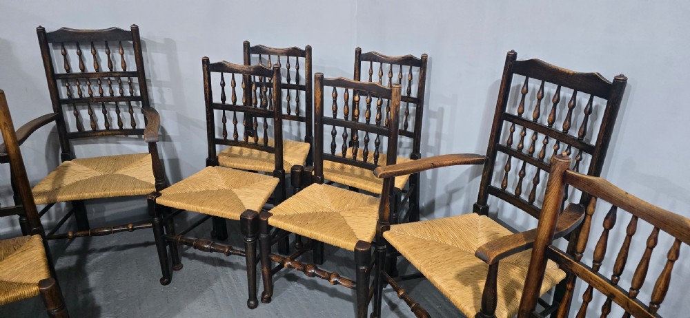 A harlequin set of eight dark oak spindle back dining chairs featuring woven rush seats, turned legs, and stretchers. View XI