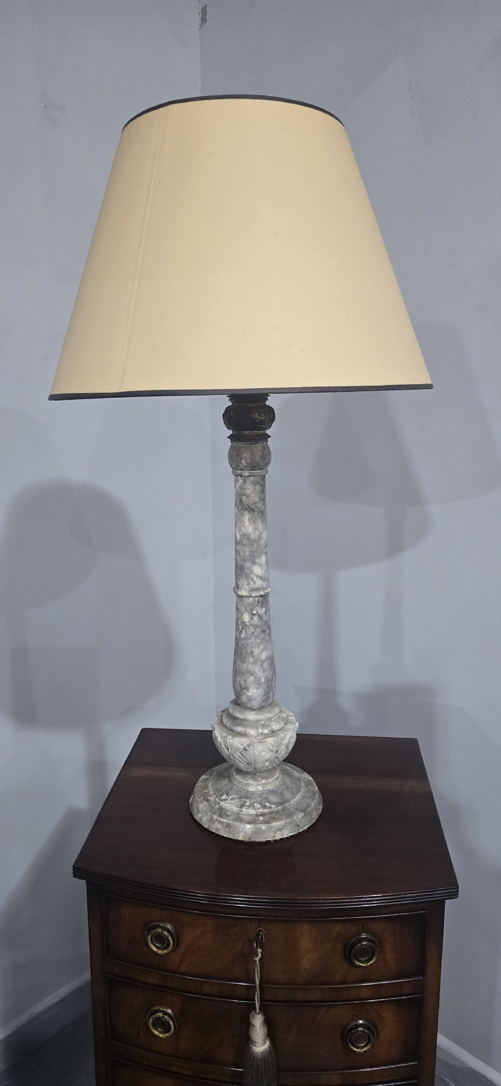 A tall grey marble turned column table lamp base with a tapered beige fabric shade bordered by dark trim. View III