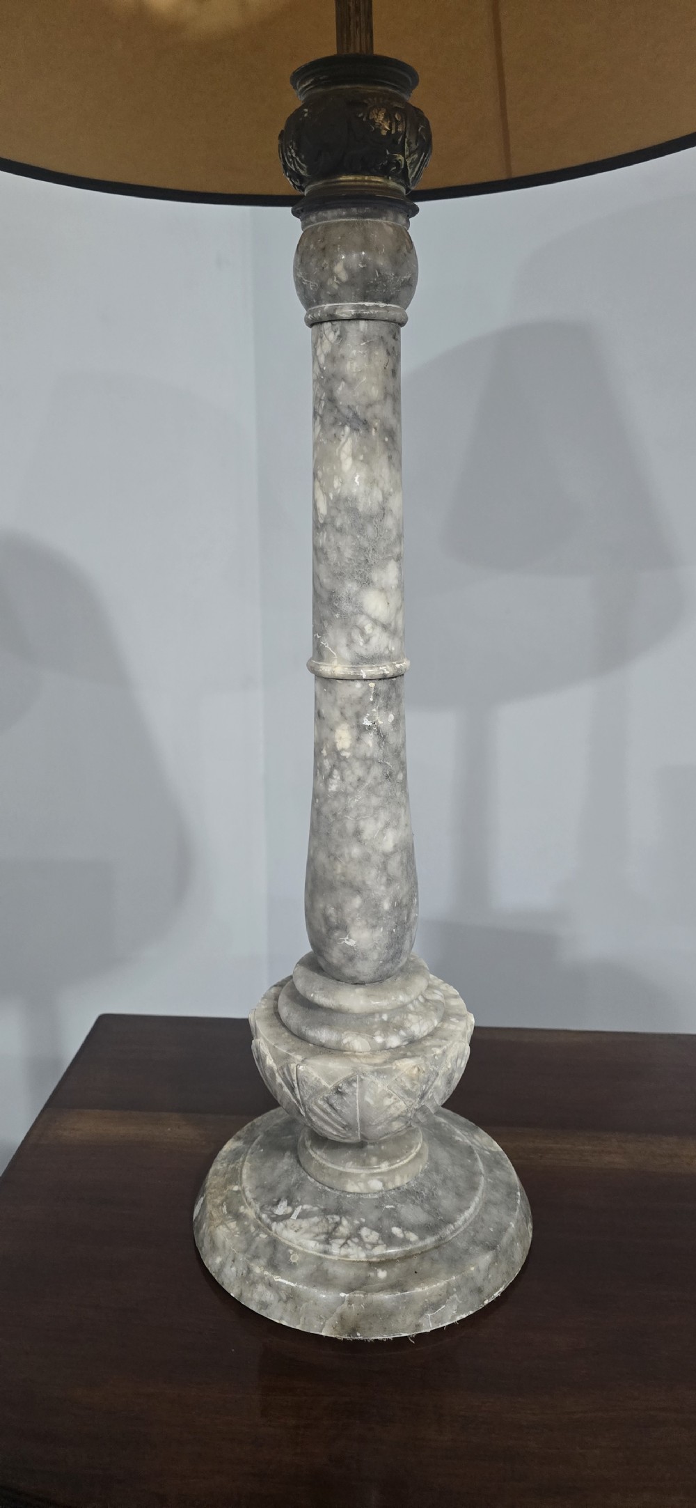 A tall grey marble turned column table lamp base with a tapered beige fabric shade bordered by dark trim. View V