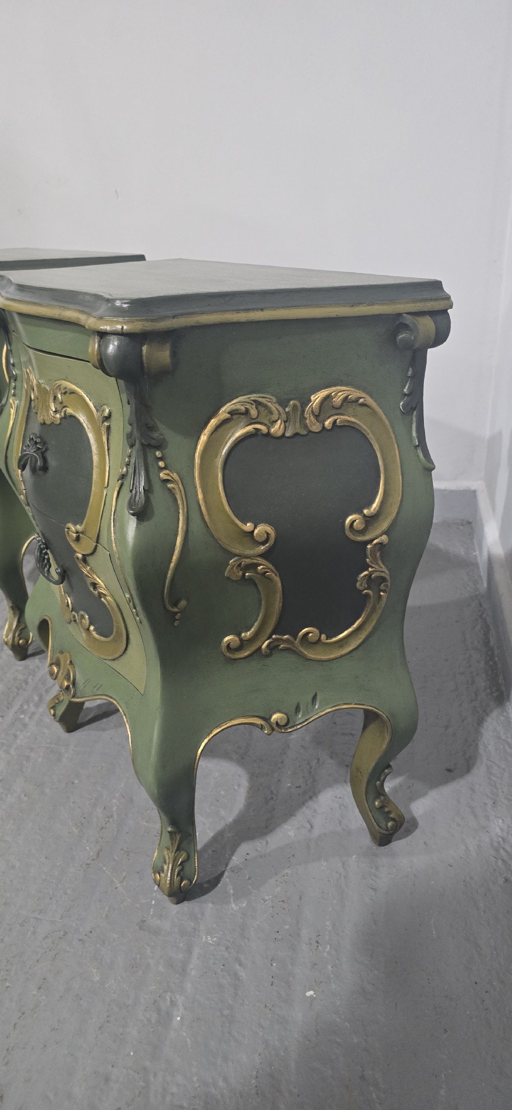 A pair of sage green and gold painted French Louis XV style bedside chests featuring bombee sides, cabriole legs, and ornate scroll moulding. View VI