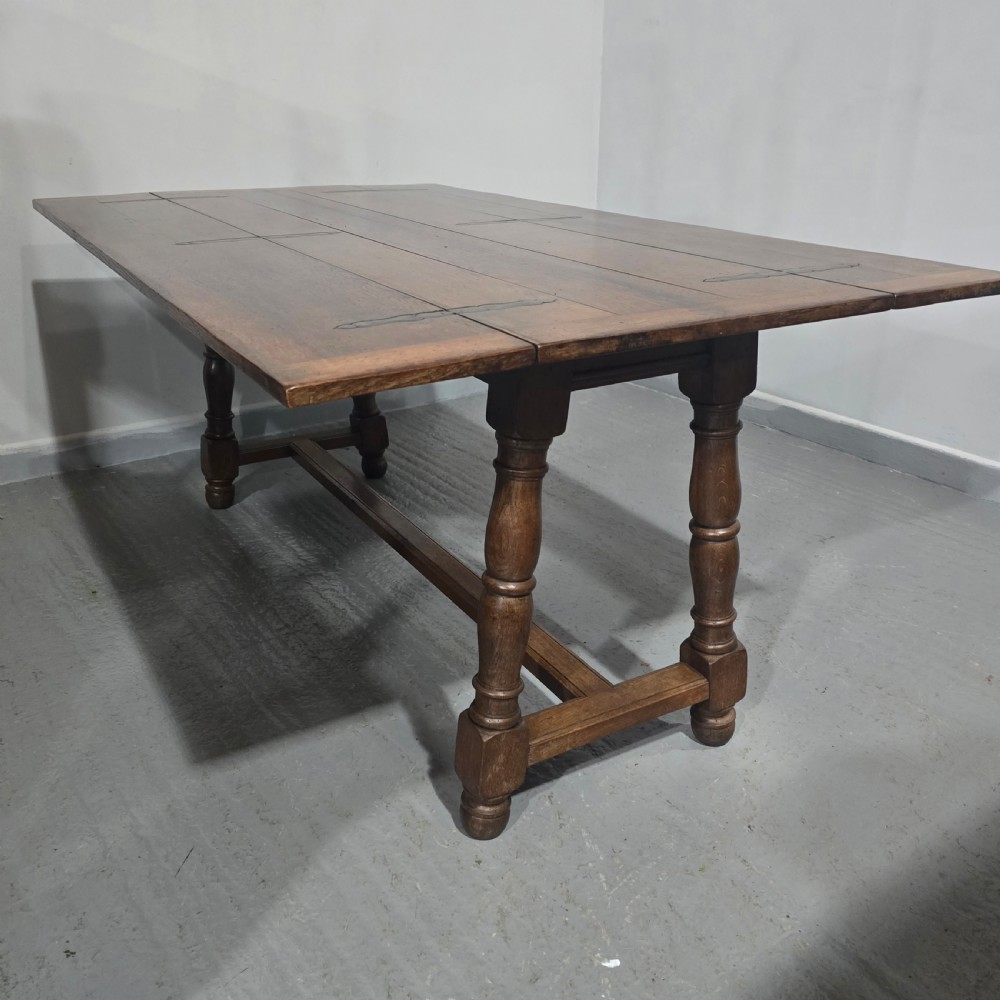 A long rectangular dark oak refectory dining table featuring turned wooden legs, a central stretcher, and a plank top. View X