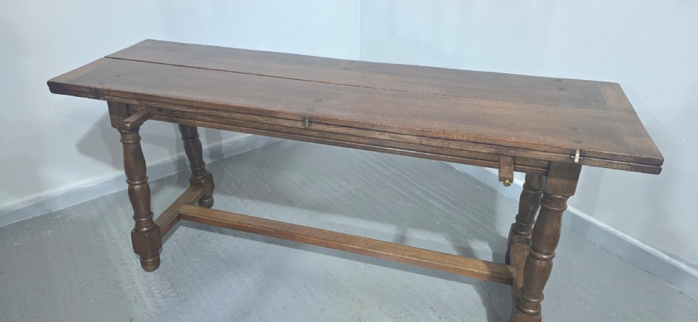 A long rectangular dark oak refectory dining table featuring turned wooden legs, a central stretcher, and a plank top. View XIV