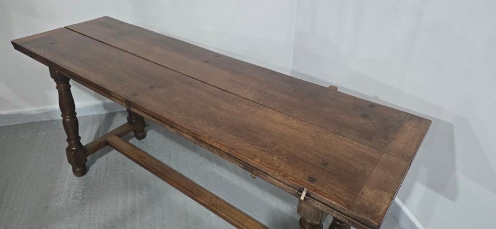A long rectangular dark oak refectory dining table featuring turned wooden legs, a central stretcher, and a plank top. View XVI