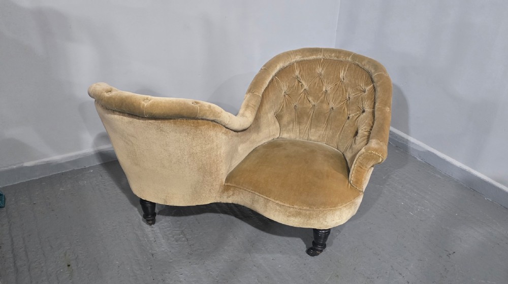 An S-shaped Victorian conversation sofa upholstered in warm gold velvet with deep-buttoned backrests and turned dark timber legs on castors. View IV