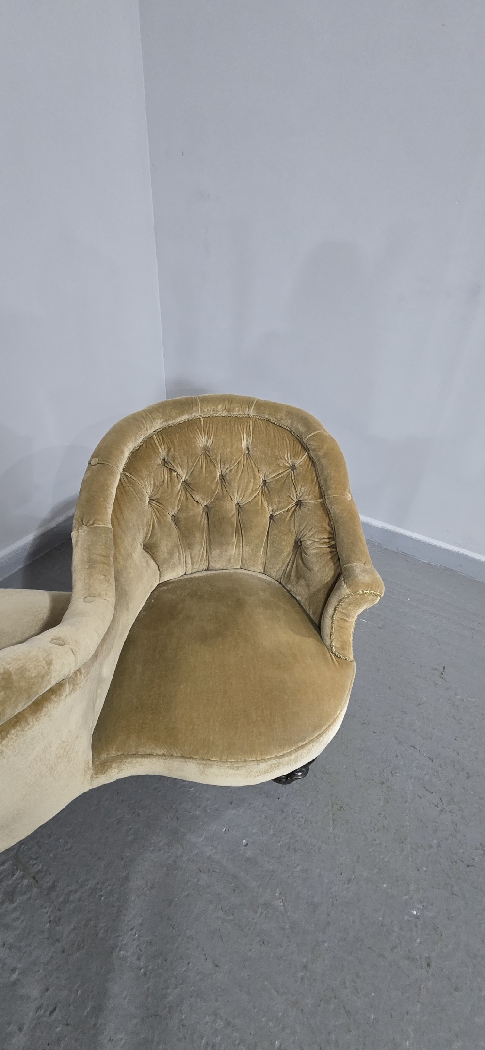 An S-shaped Victorian conversation sofa upholstered in warm gold velvet with deep-buttoned backrests and turned dark timber legs on castors. View VII