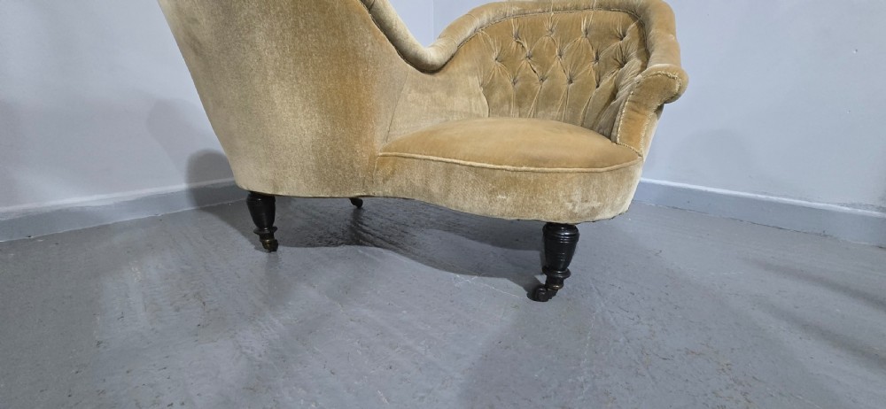 An S-shaped Victorian conversation sofa upholstered in warm gold velvet with deep-buttoned backrests and turned dark timber legs on castors. View XIII