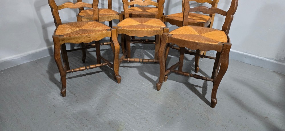 A set of six French rustic oak dining chairs featuring wavy ladderbacks, natural woven rush seats, and front cabriole legs. View III