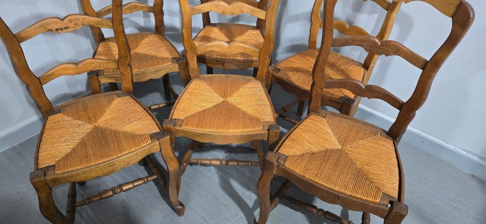 A set of six French rustic oak dining chairs featuring wavy ladderbacks, natural woven rush seats, and front cabriole legs. View IV
