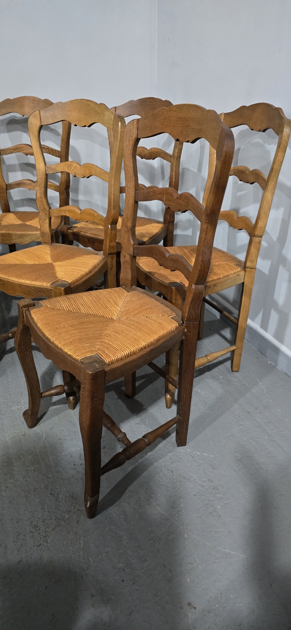 A set of six French rustic oak dining chairs featuring wavy ladderbacks, natural woven rush seats, and front cabriole legs. View V
