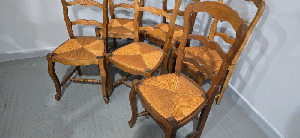 A set of six French rustic oak dining chairs featuring wavy ladderbacks, natural woven rush seats, and front cabriole legs. View VI
