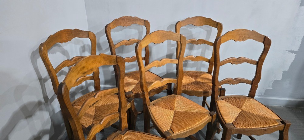 A set of six French rustic oak dining chairs featuring wavy ladderbacks, natural woven rush seats, and front cabriole legs. View VII