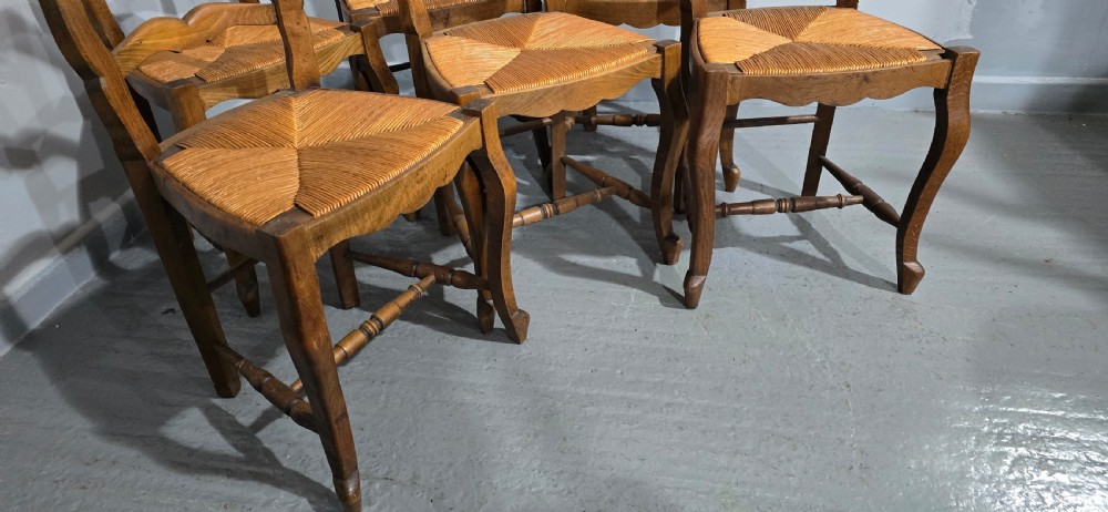 A set of six French rustic oak dining chairs featuring wavy ladderbacks, natural woven rush seats, and front cabriole legs. View VIII