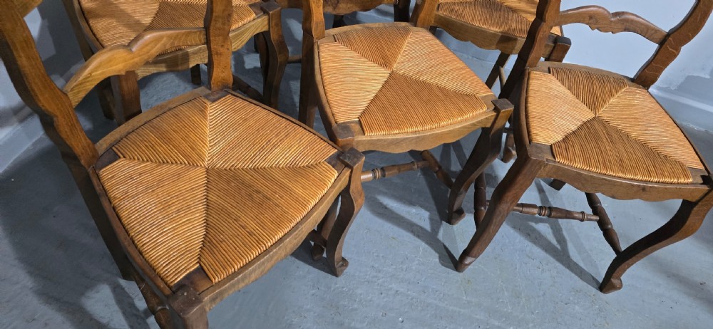 A set of six French rustic oak dining chairs featuring wavy ladderbacks, natural woven rush seats, and front cabriole legs. View IX