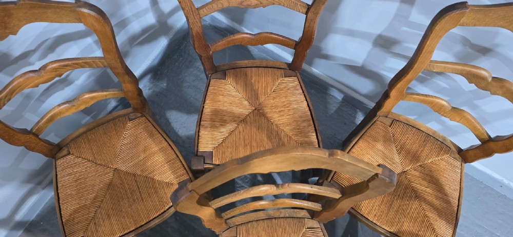 A set of six French rustic oak dining chairs featuring wavy ladderbacks, natural woven rush seats, and front cabriole legs. View X