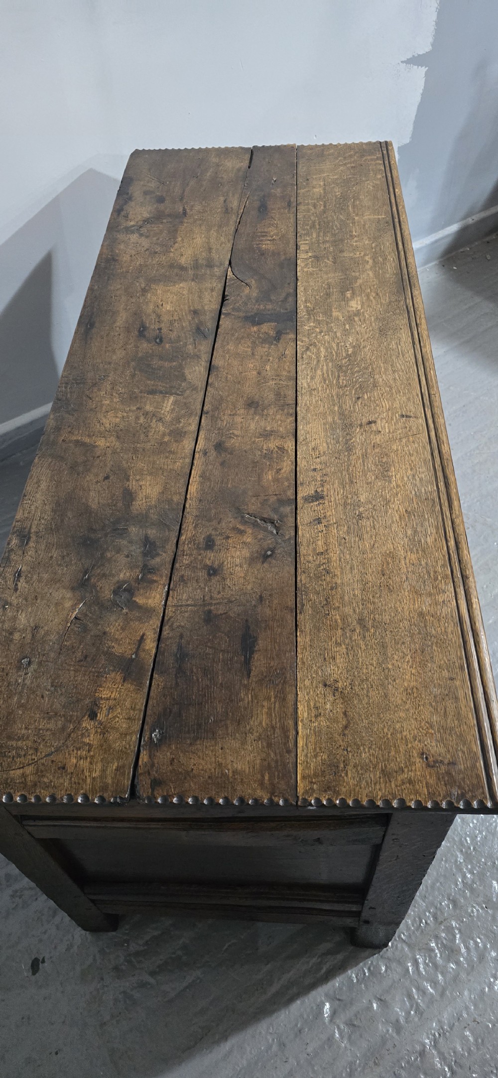 A dark brown Georgian oak coffer featuring a rectangular hinged lid, three recessed front panels, horizontal moulded rails, and an iron lock plate. View VI