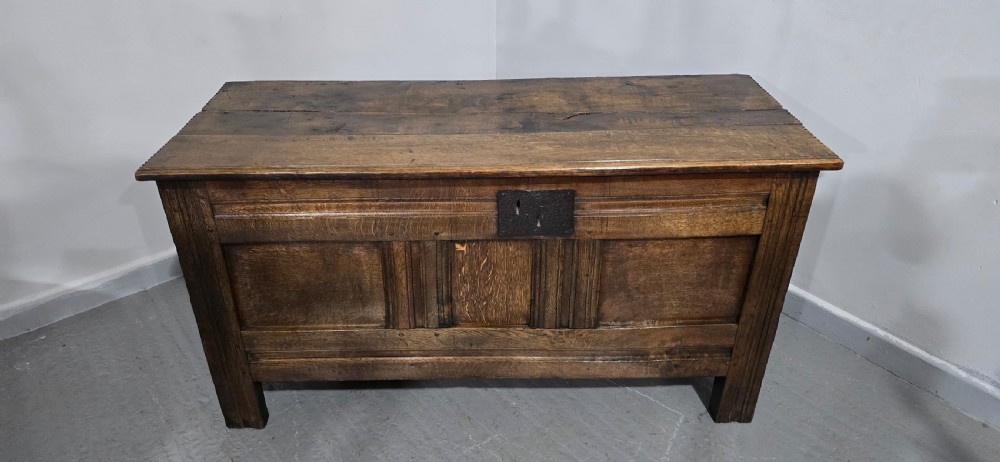 A dark brown Georgian oak coffer featuring a rectangular hinged lid, three recessed front panels, horizontal moulded rails, and an iron lock plate. View XII