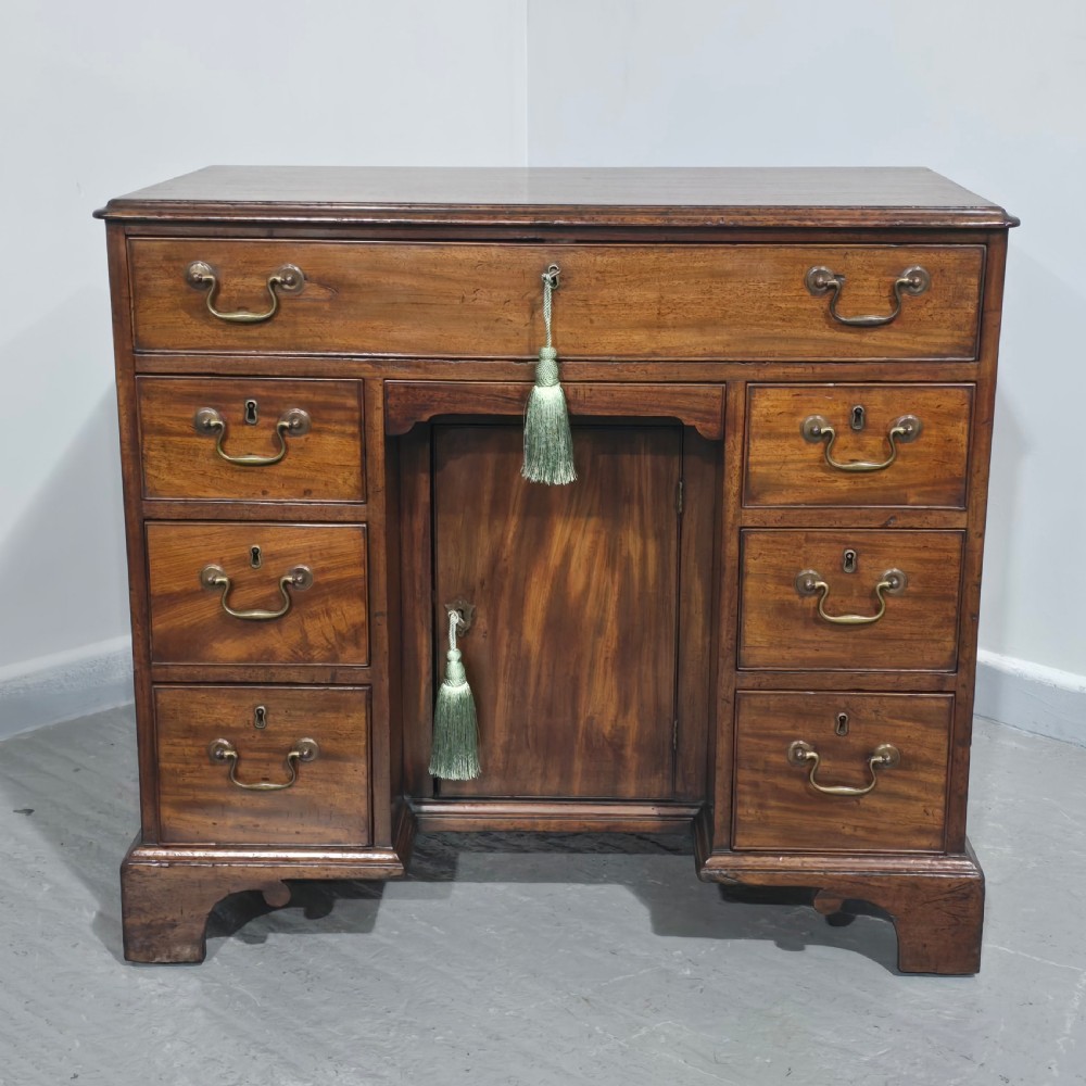 A Georgian mahogany kneehole desk featuring a long top drawer, six side drawers, a central recessed cupboard, brass swan-neck handles, and bracket feet. View II