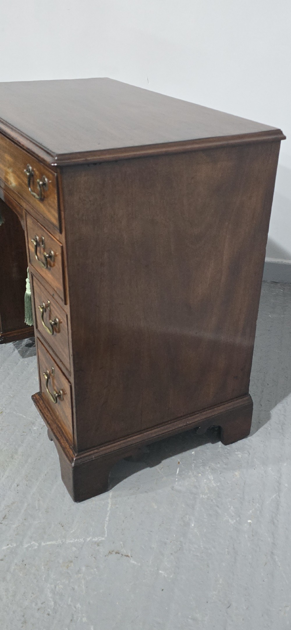 A Georgian mahogany kneehole desk featuring a long top drawer, six side drawers, a central recessed cupboard, brass swan-neck handles, and bracket feet. View IV