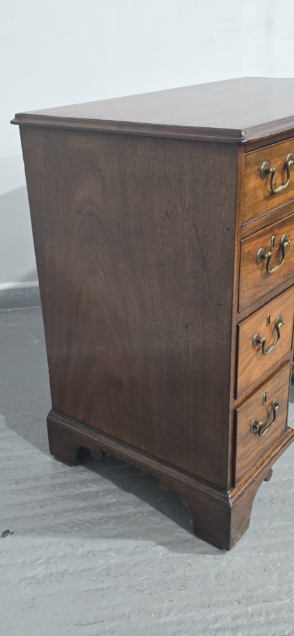 A Georgian mahogany kneehole desk featuring a long top drawer, six side drawers, a central recessed cupboard, brass swan-neck handles, and bracket feet. View V