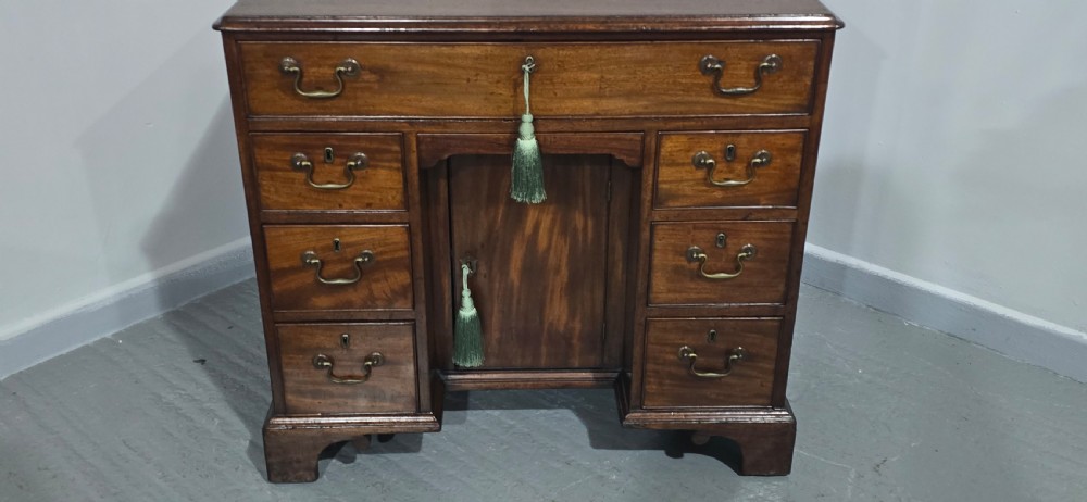 A Georgian mahogany kneehole desk featuring a long top drawer, six side drawers, a central recessed cupboard, brass swan-neck handles, and bracket feet. View VII