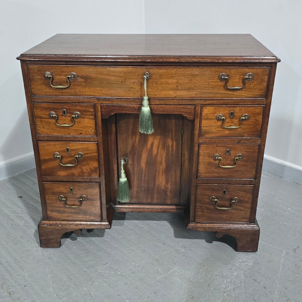 A Georgian mahogany kneehole desk featuring a long top drawer, six side drawers, a central recessed cupboard, brass swan-neck handles, and bracket feet. View VIII