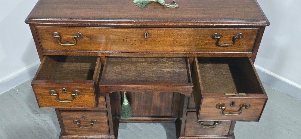A Georgian mahogany kneehole desk featuring a long top drawer, six side drawers, a central recessed cupboard, brass swan-neck handles, and bracket feet. View X