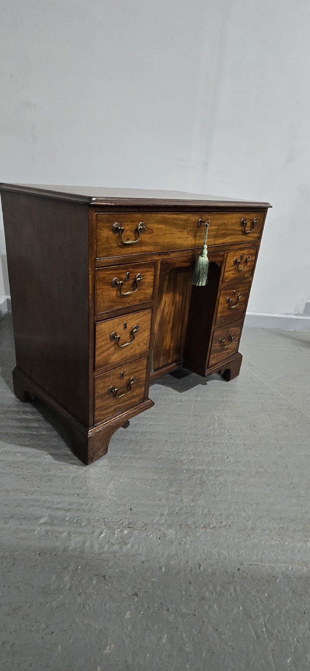 A Georgian mahogany kneehole desk featuring a long top drawer, six side drawers, a central recessed cupboard, brass swan-neck handles, and bracket feet. View XVII