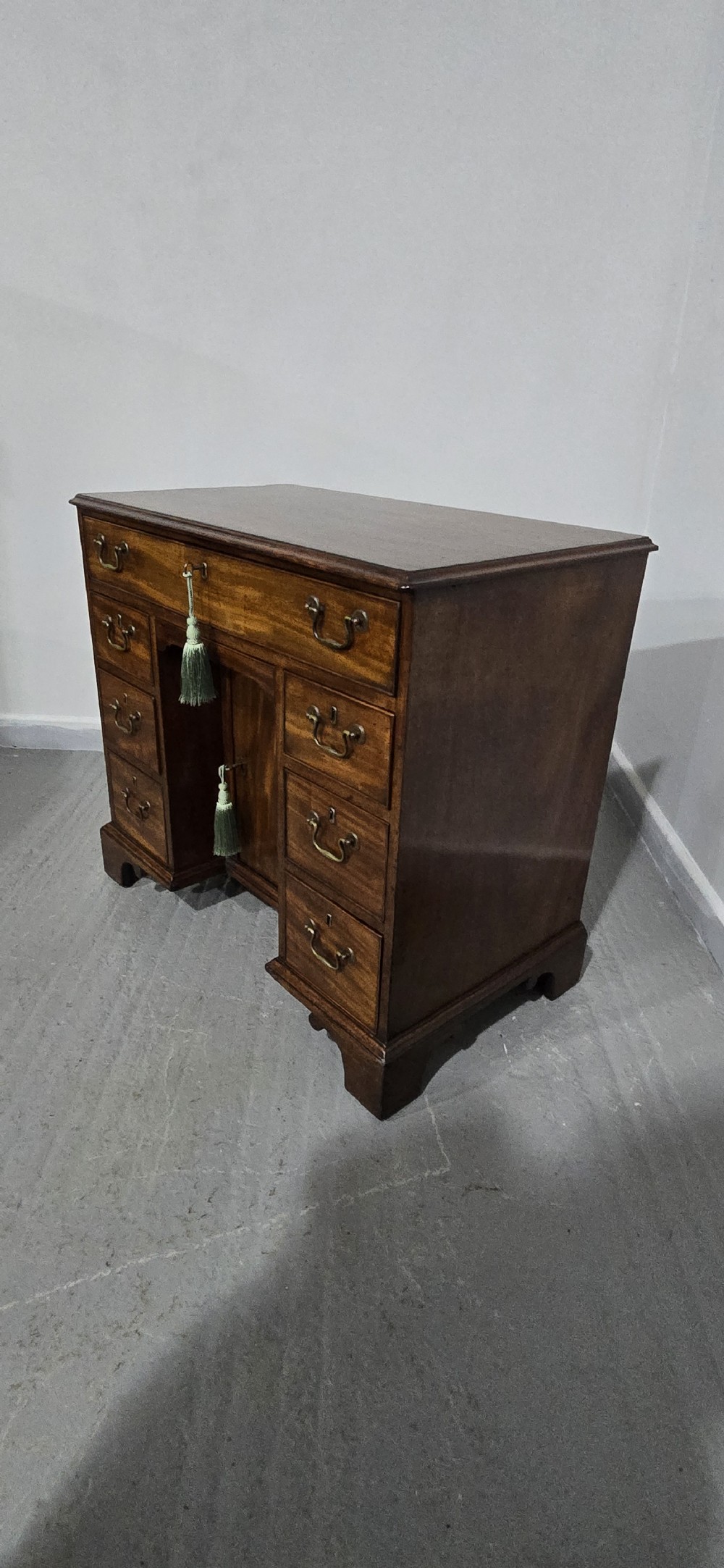 A Georgian mahogany kneehole desk featuring a long top drawer, six side drawers, a central recessed cupboard, brass swan-neck handles, and bracket feet. View XVIII