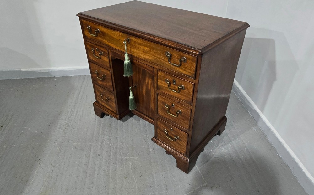 A Georgian mahogany kneehole desk featuring a long top drawer, six side drawers, a central recessed cupboard, brass swan-neck handles, and bracket feet. View XIX