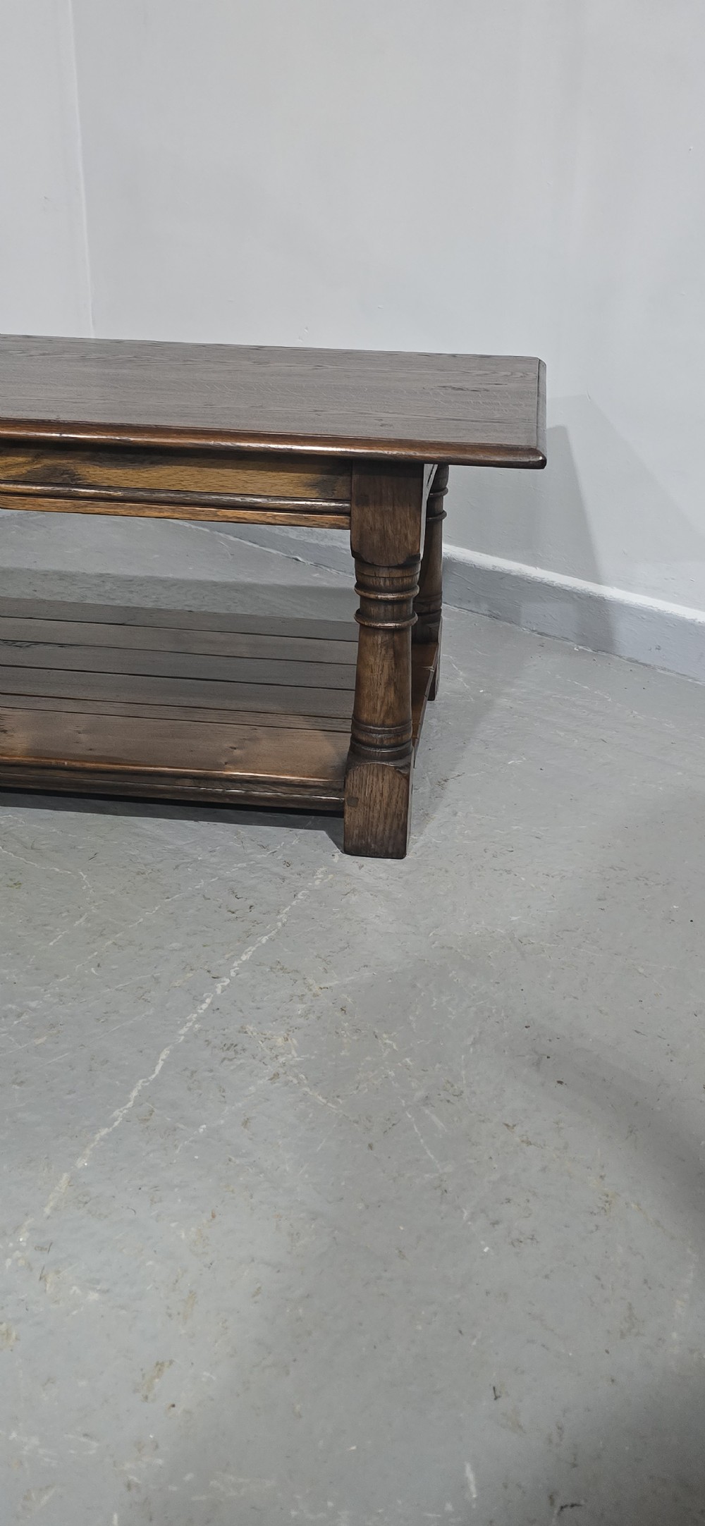 A rectangular dark oak coffee table featuring a plank top, turned legs, and a lower slatted shelf. View VI